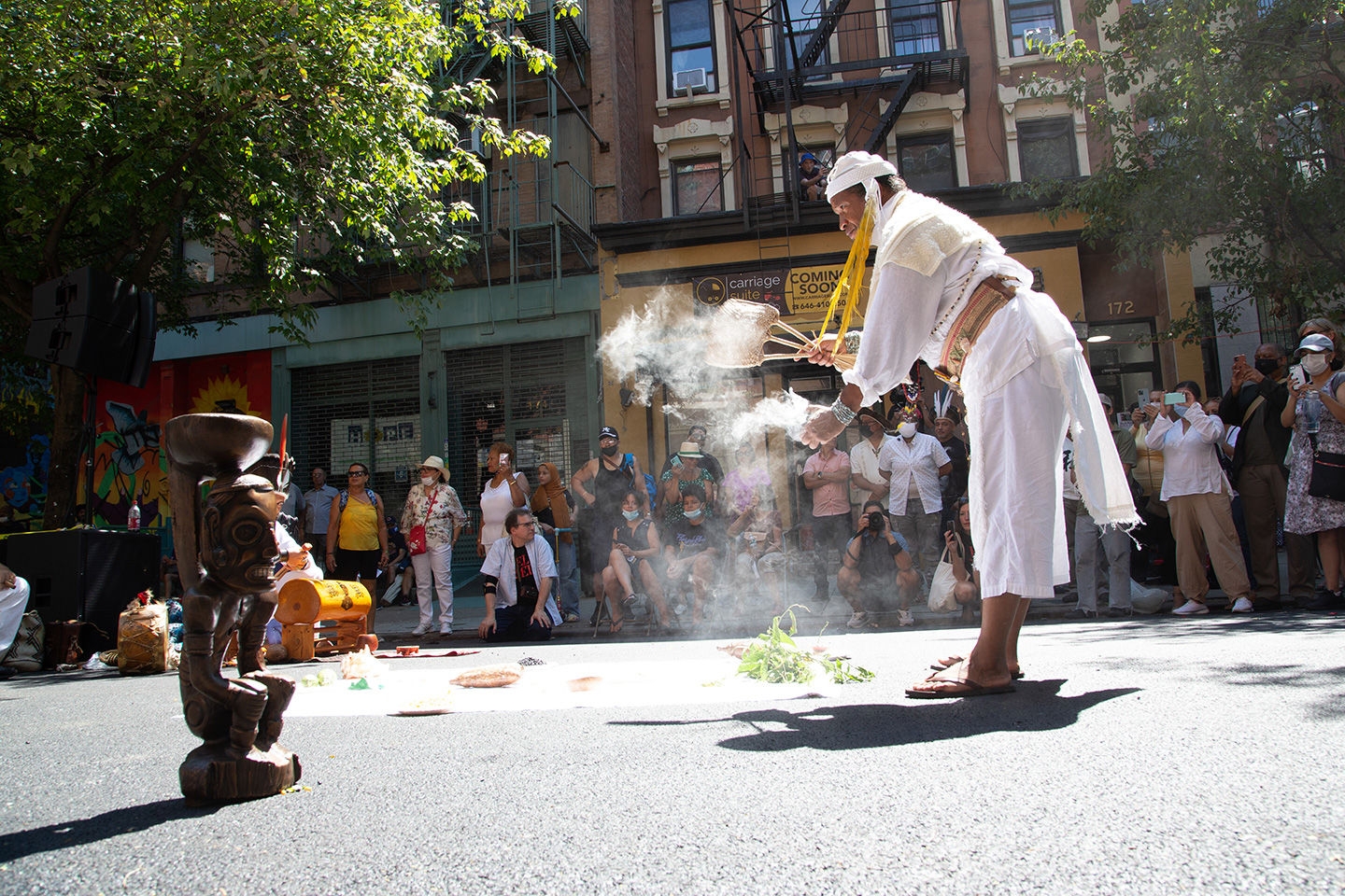 A crowd watches as a member of the Caney Indigenious Spiritual Circle performs a ritual with a replica of a Cemí Cohobabat stand at Miguel Luciano’s culminating community event in El Barrio.